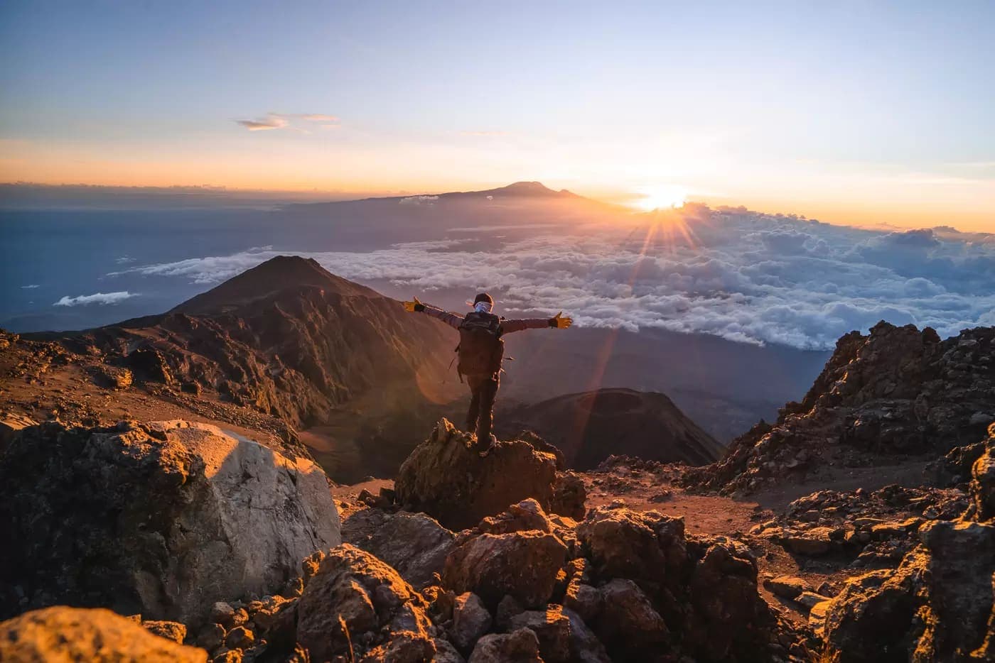 A hiker on a rocky summit above the clouds at sunrise
