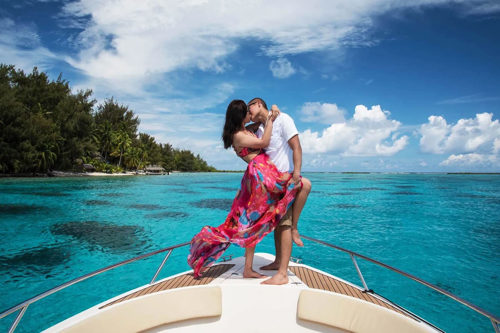 A couple on a boat beside a palm-lined coast