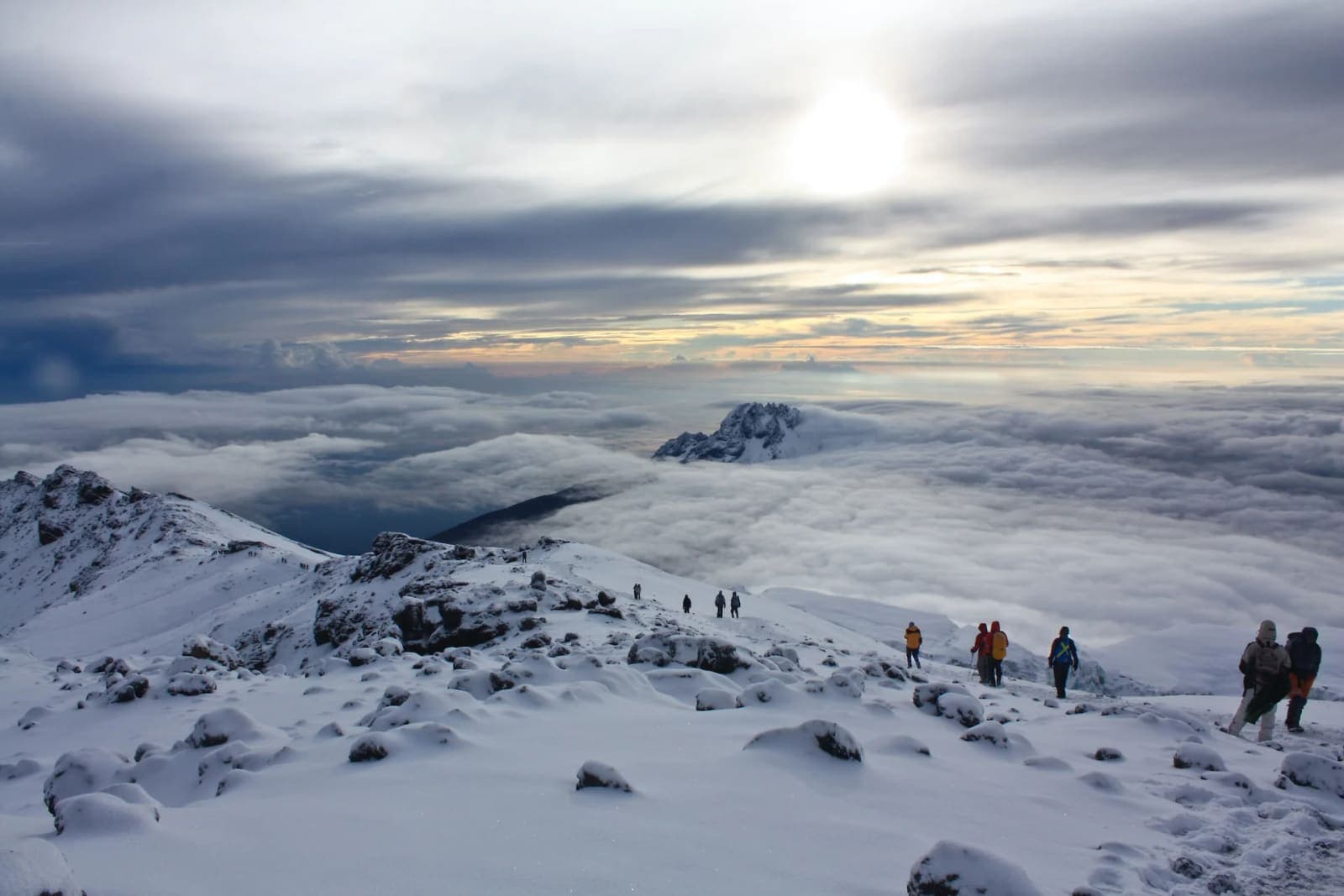 Climbers on a snowy ridge above the clouds